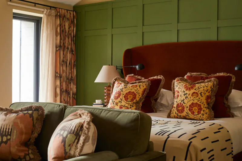 Elegant bedroom at Rothay Manor with green paneled walls, red velvet headboard, floral pillows, and large window.