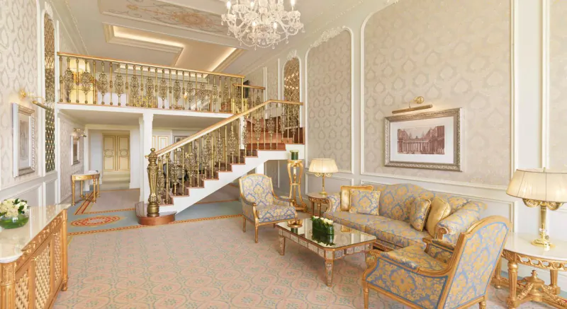 Opulent Raffles The Palm Dubai lobby with grand white staircase, gold railings, chandelier, and plush blue armchairs.