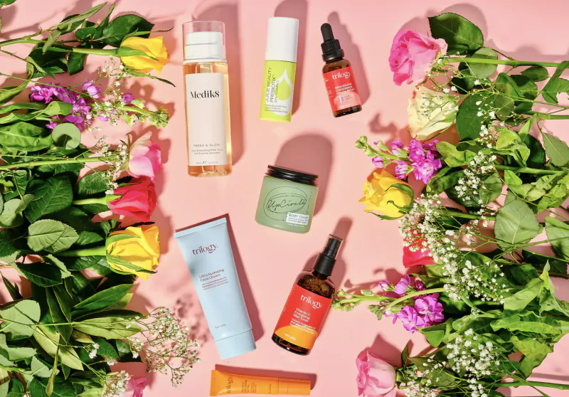 Assortment of Nulala skincare products including bottles, jars, and creams arranged on pink surface with colorful flowers