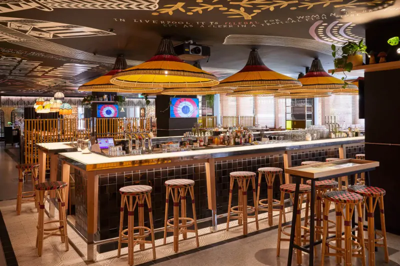 Stylish bar interior with orange pendant lamps, wooden stools, neon screens, and plants for Halloween fun at Mama London Gallery