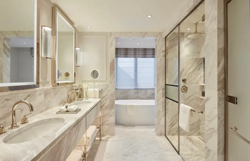 Luxurious modern bathroom in Carlton Tower Jumeirah with marble vanity, freestanding tub, glass shower, and large mirrors.