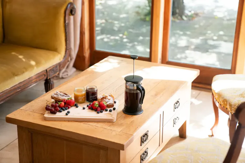 Elegant breakfast tray on wooden table: berries, waffles, jam, French press coffee, by window in Cotswolds house.