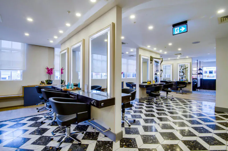 Modern Jo Hansford hair salon with black swivel chairs at white mirrored stations on chequerboard floor, orchids and exit sign.