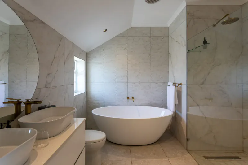 Modern luxury bathroom with freestanding white bathtub, double vanities, glass shower, marble tiles at Abalone Hotel.