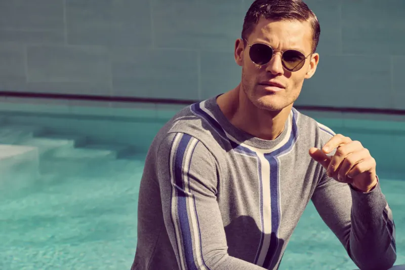 Man in gray long-sleeve shirt with blue stripes poses confidently by pool in Holmby Hills Collection.