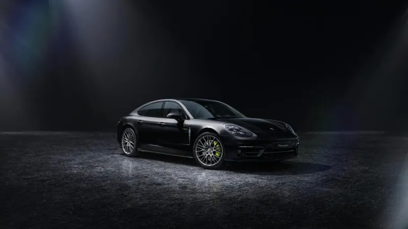 Black Porsche Panamera Platinum Edition sedan on dark studio floor with spotlight glow and lens flare