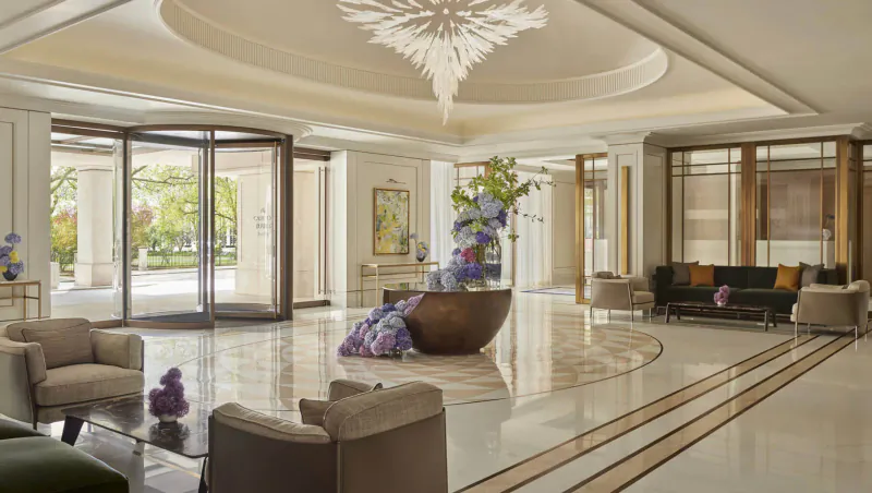 Elegant Carlton Tower Jumeirah Hotel lobby in London with chandelier, purple flower arrangements, seating, and entrance.