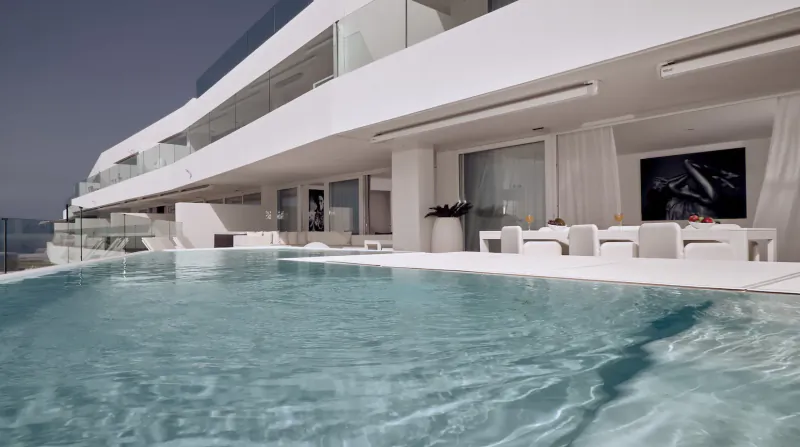 Infinity pool and white modern terrace at Baobab Suites resort in Tenerife, with lounge chairs and sea view.