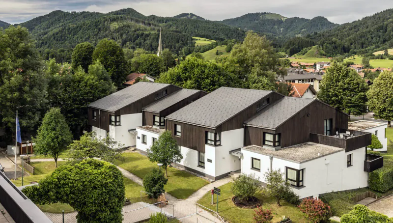 Aerial view of modern white and dark-roofed chalets at Karma Bavaria resort amid green Bavarian Alps and forests, Schliersee, Germany.