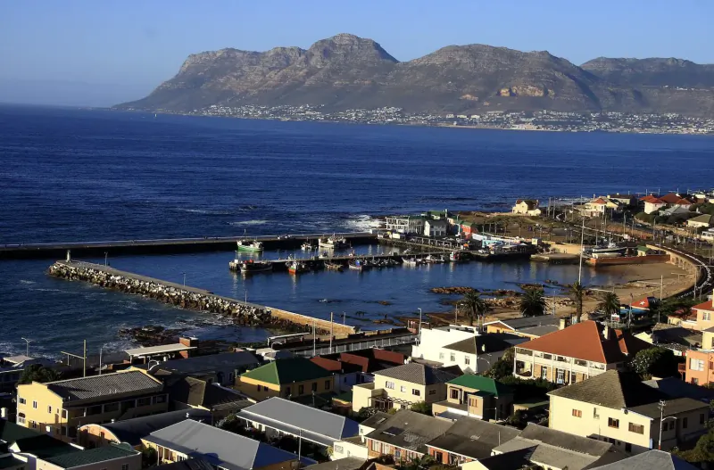 Aerial view of Kalk Bay harbour in Cape Town, with fishing boats, colorful village homes, and Table Mountain backdrop.