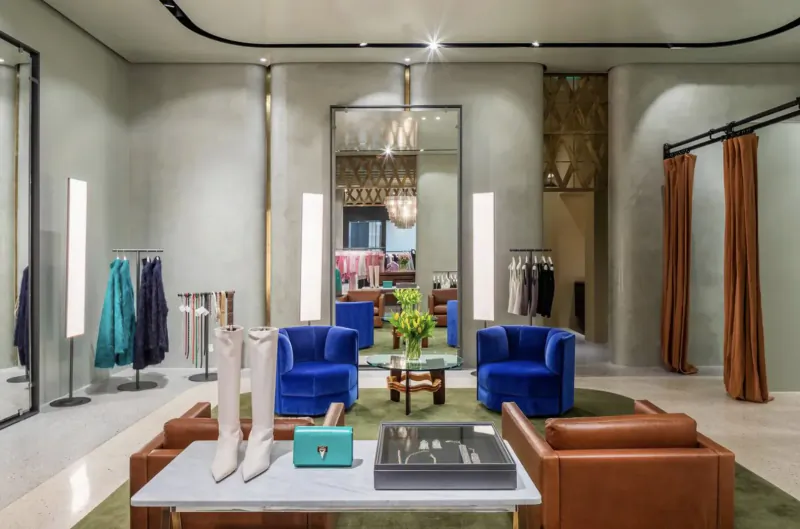 Scanlan Theodore luxury fashion gallery with blue boots and handbag on table amid velvet chairs, clothing racks, and large mirror