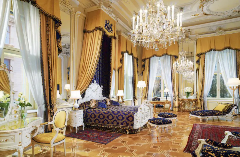 Opulent Hotel Imperial Vienna bedroom with ornate canopy bed, gold drapes, chandeliers, and antique furniture.