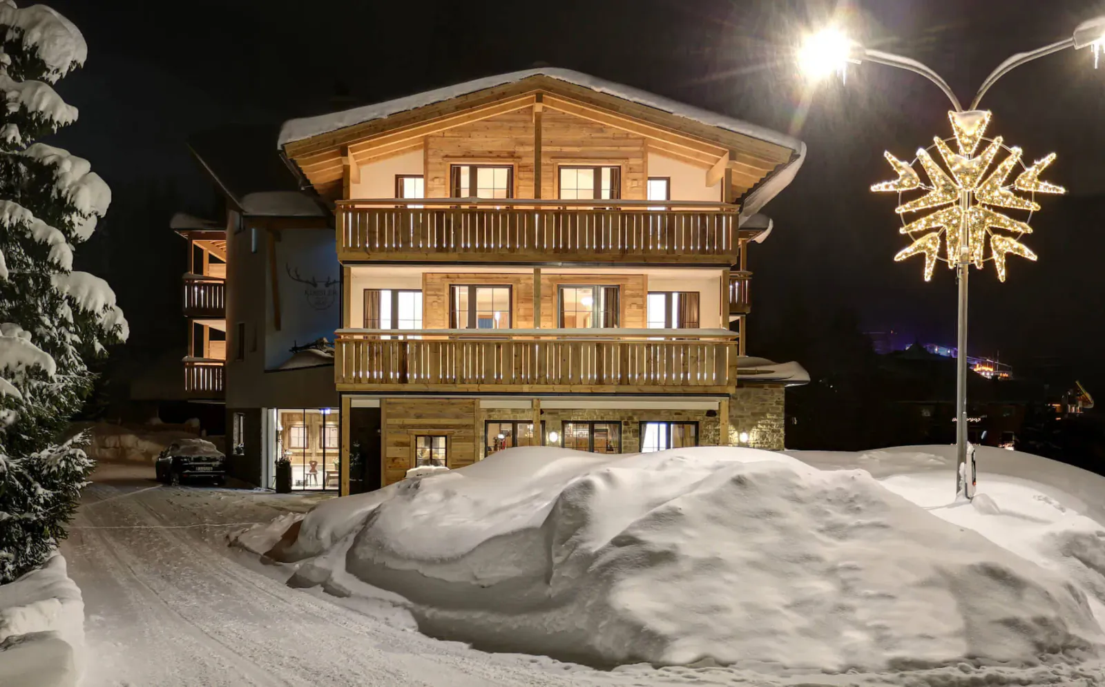 Hotel Kösslerhof, a lit wooden chalet in snowy St Anton am Arlberg at night with star lights and lamps.