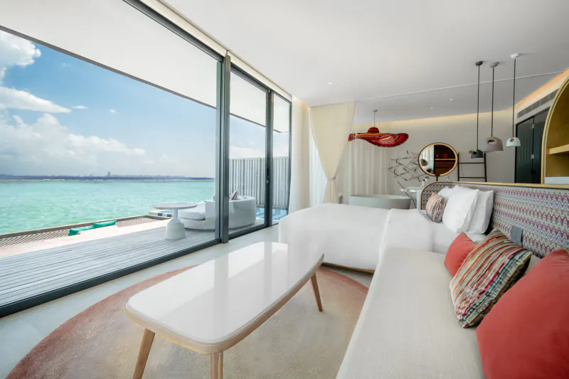 Luxurious beachfront villa at Crossroads Maldives with panoramic turquoise ocean view, modern white sofa, red pillows, and curved decor.