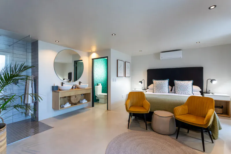 Spacious Oyster Suite at Abalone Hotel with king bed, yellow chairs, open glass shower, and plants.