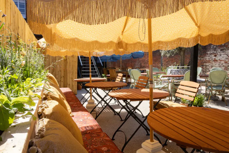 Outdoor seating at The George & Dragon Marlow: fringed yellow umbrellas, wooden tables, green chairs, plants, brick wall, stairs.