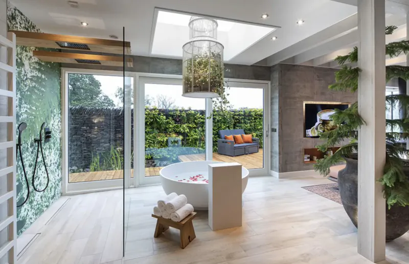 Luxurious modern bathroom at Gilpin Hotel with freestanding tub, plants, skylight, and garden view