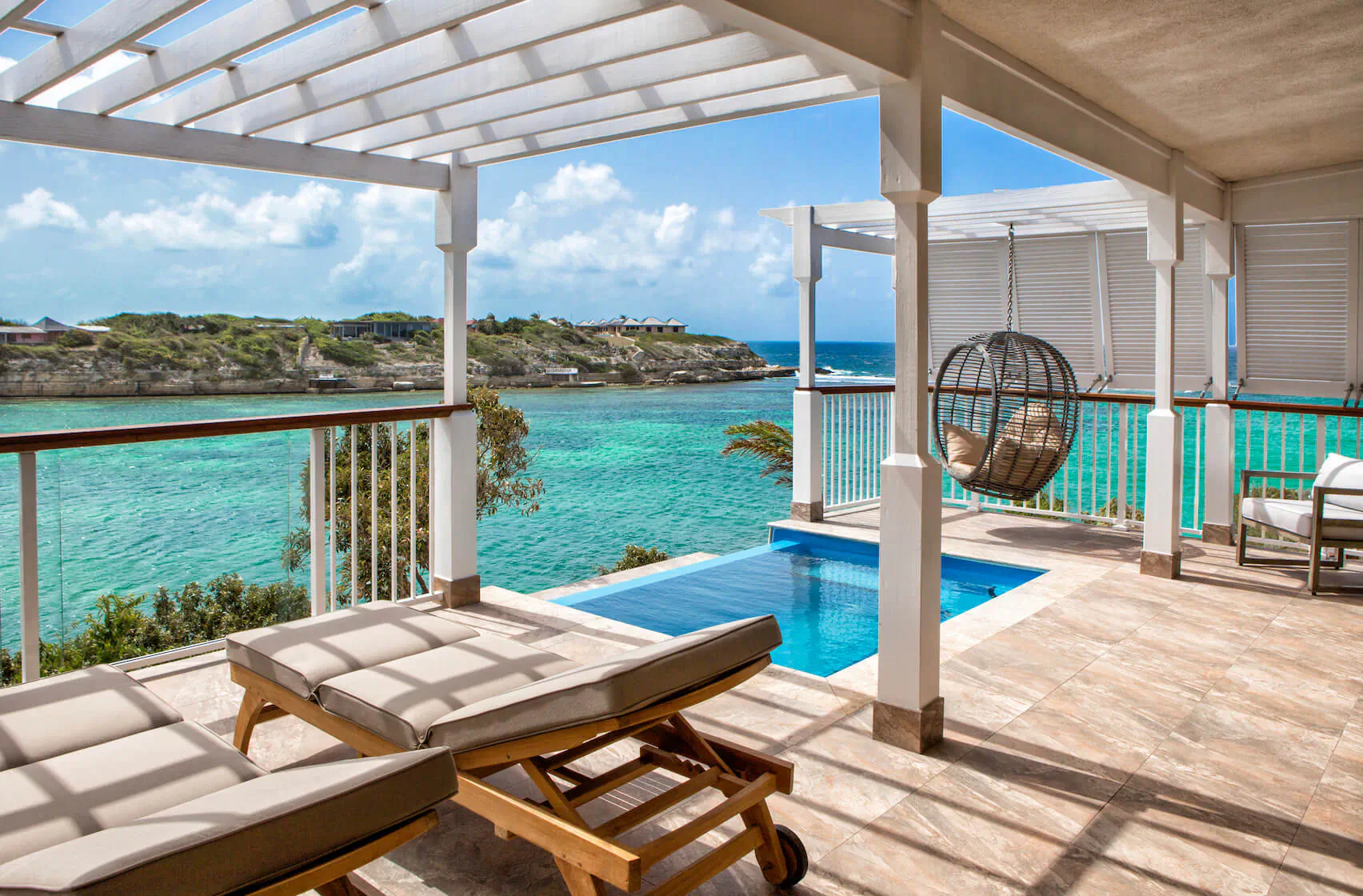 Luxury villa terrace at Hammock Cove, Antigua: infinity pool, swing chair, loungers overlooking turquoise sea and hills.