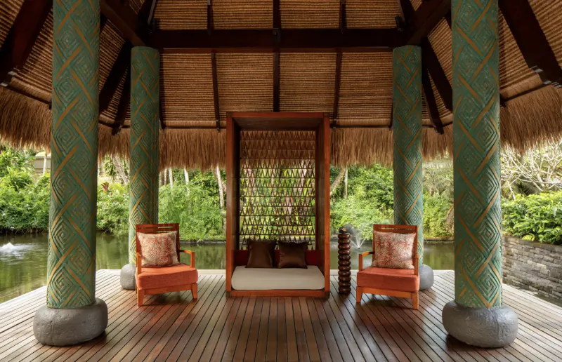 Open-air thatched pavilion with orange chairs and daybed on wooden deck over jungle pond at Anantara Maia Seychelles Villas