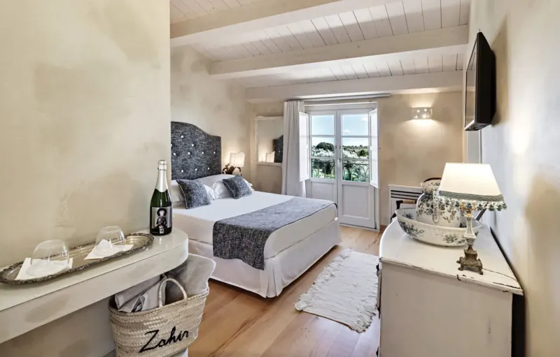 Elegant bedroom at Zahir Country House with tufted bed, champagne bottle, balcony view, and rustic Sicilian decor
