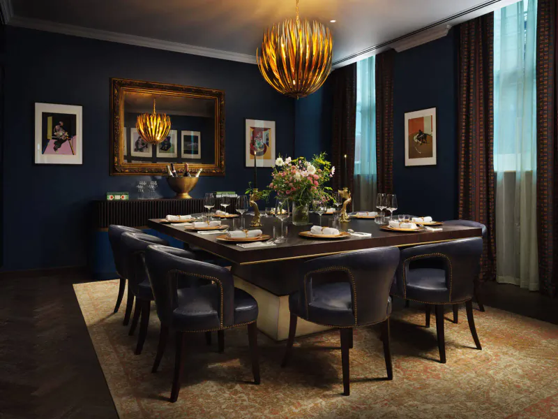 Elegant navy dining room with gold chandelier, set table, leather chairs, art, and flowers.