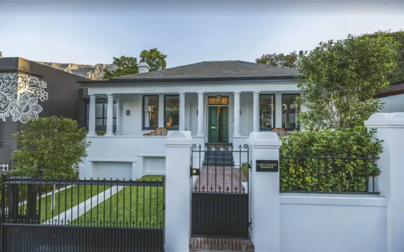 Cape Cadogan Boutique Hotel facade: white colonial house with green door, pillars, black gate, lush gardens, Cape Town.