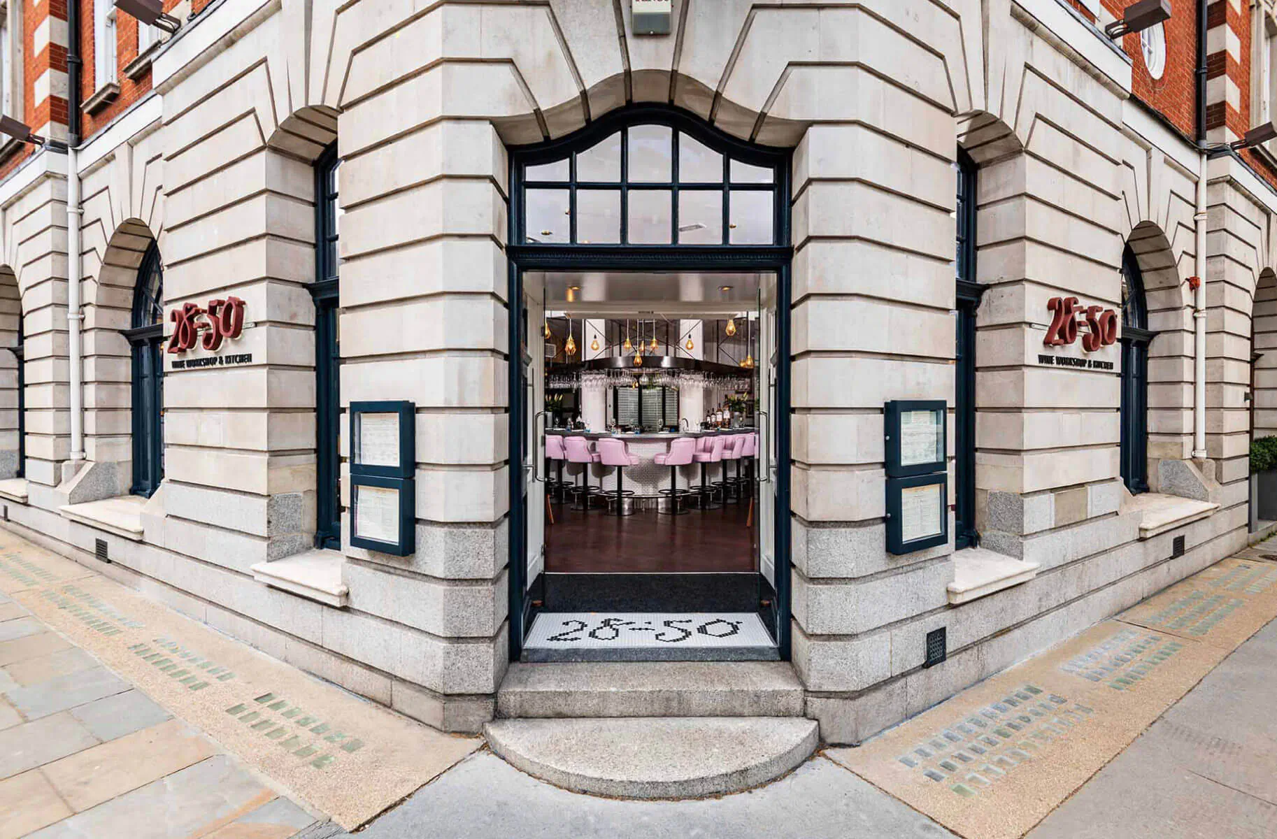 28°-50° Chelsea restaurant exterior with ornate stone facade, open door revealing pink chairs at tables inside, red signage, on street corner
