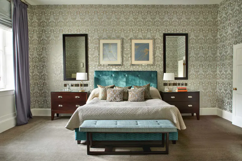Elegant bedroom in Home House club with teal velvet bed, matching bench, mirrors, and damask wallpaper.