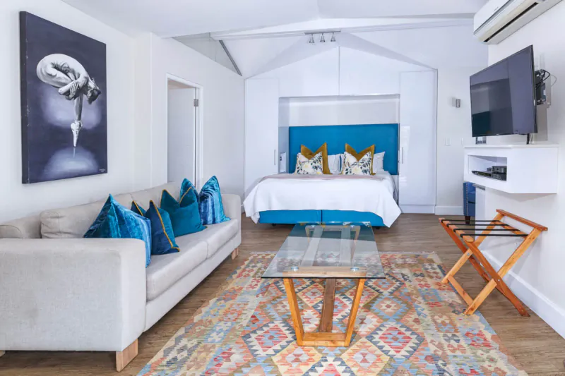 Cozy Turbine Boutique Hotel room with teal headboard bed, gray sofa, glass coffee table on patterned rug, black and white flower art, TV.