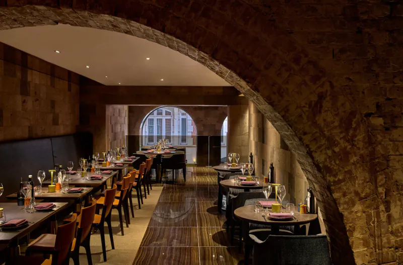 Elegant dining room at Lusin Mayfair with arched stone walls, set tables, and large window.