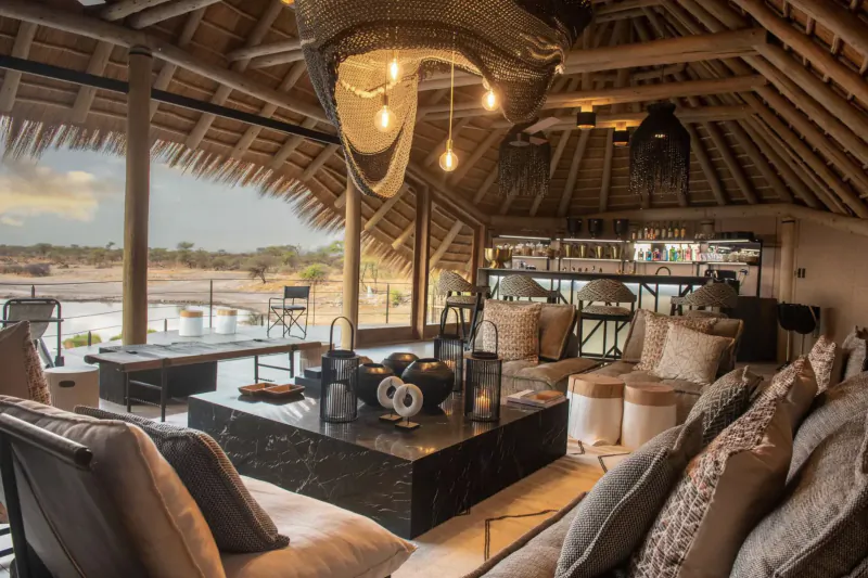 Luxurious thatched lounge at Camp Kala with black stone table, plush cushions, and Etosha views at sunset.