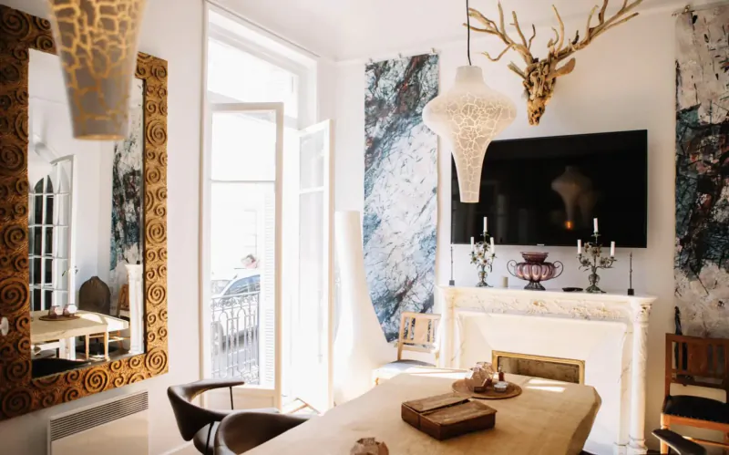 Elegant living room in Manon Les Suites with wooden table, antler decor, ornate mirrors, TV, and balcony doors