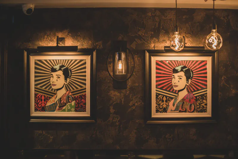 Two framed pop art portraits of women in kimonos on restaurant wall with lanterns and warm lighting