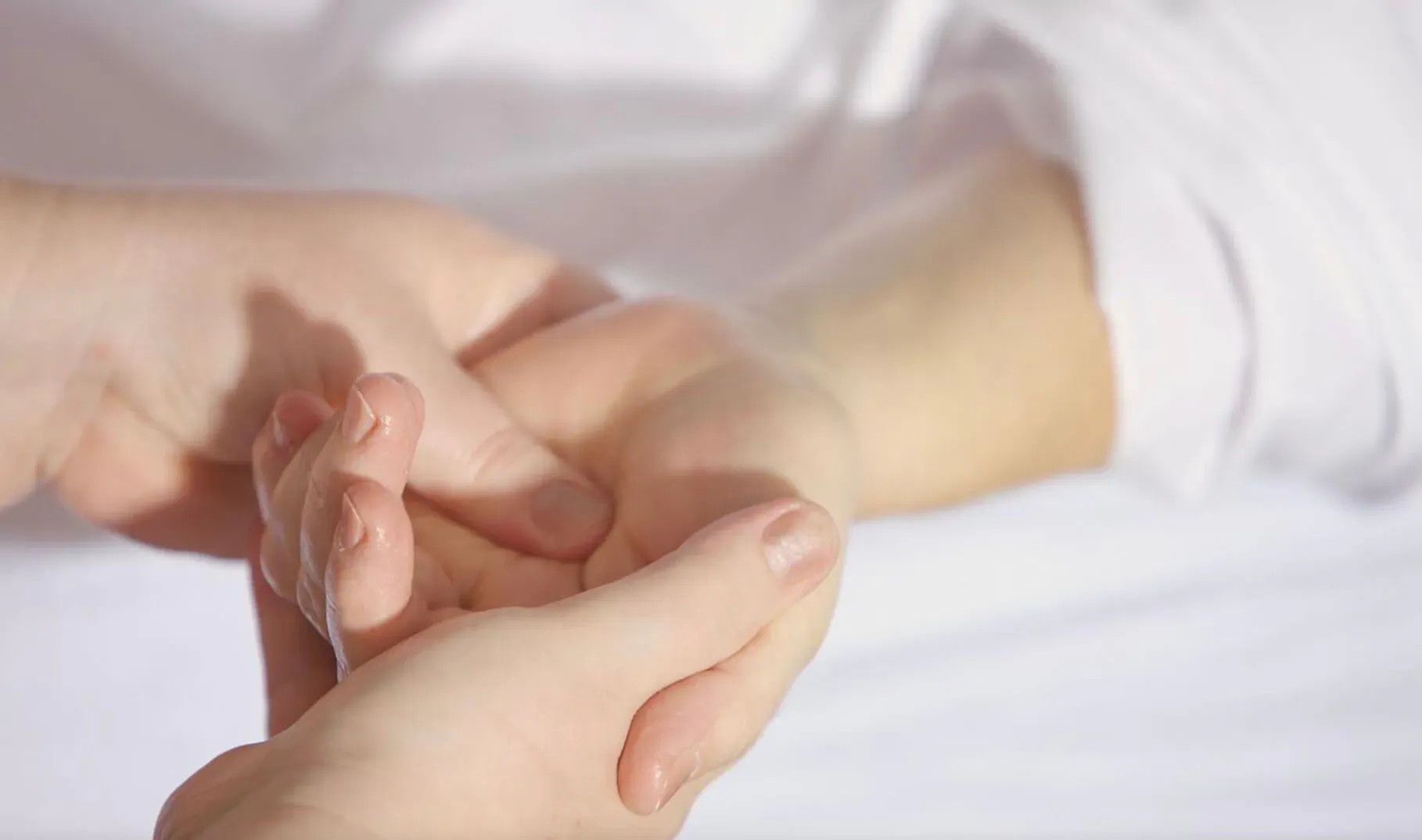 Close-up of hands gently massaging a wrist on a white surface, highlighting skin texture.