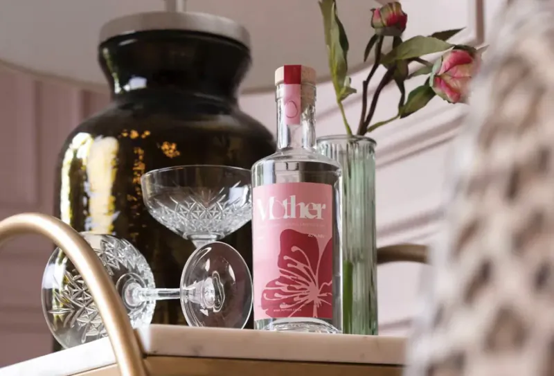 Pink 'Älskar' gin bottle with etched glasses, roses, and vase on gold tray