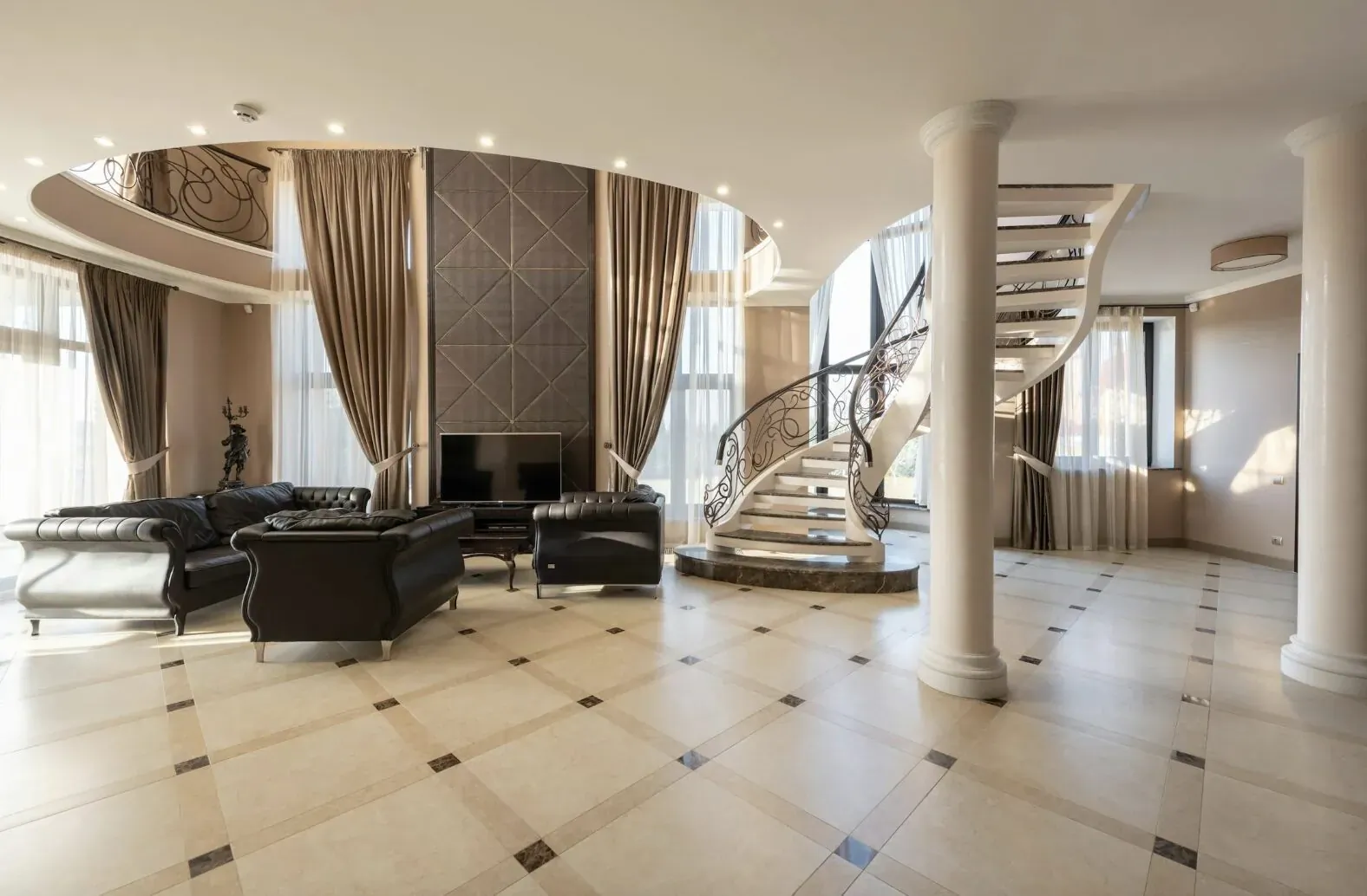 Luxurious modern living room with black leather sofas, fireplace, and curved glass staircase