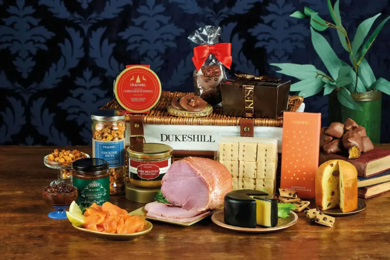 Dukeshill Christmas hamper on wooden table with ham, cheeses, chocolates, nuts, and festive foods