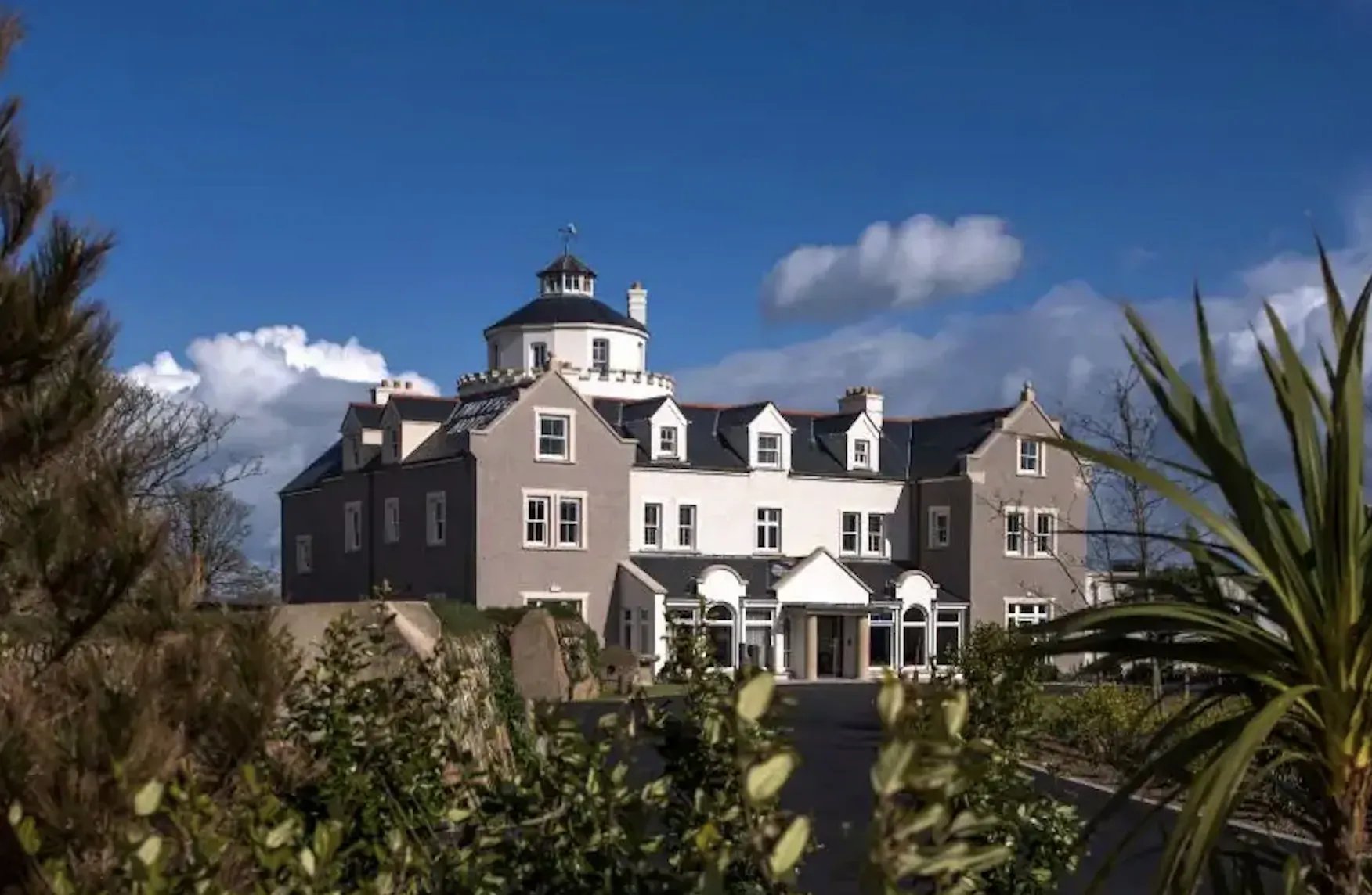 Twr y Felin, Wales' first contemporary art hotel, a grand gray mansion with dome tower, surrounded by trees under blue sky.