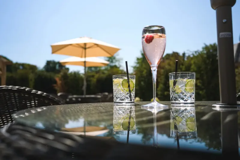 Outdoor table at Manor House Hotel with pink strawberry gin fizz and lime gin & tonics under beige umbrellas on sunny patio.