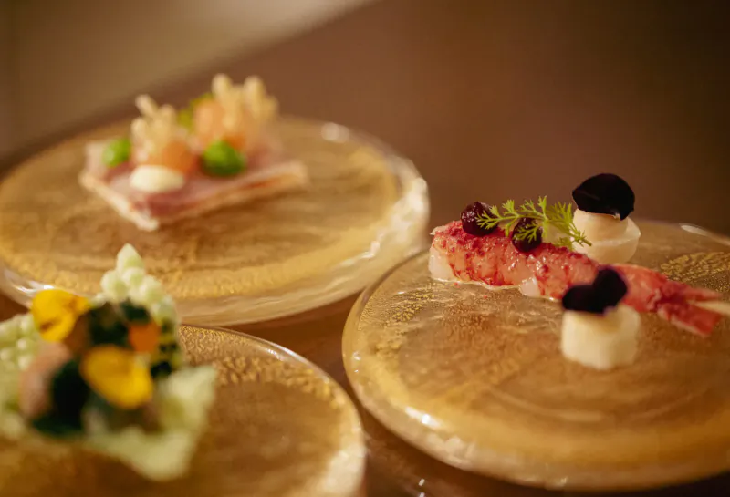 Three elegant plates on gold stands: shrimp with garnishes, ham with peas, and mushrooms with veggies.
