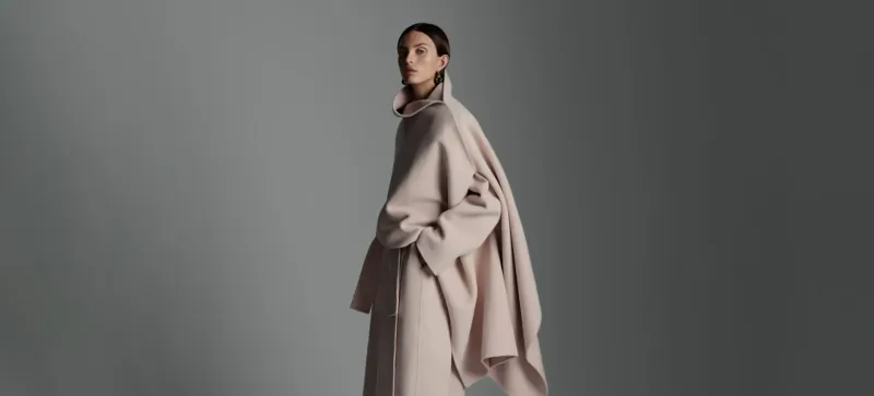 Model in profile view wearing flowing pale pink Scanlan Theodore coat, quiet luxury fashion on gray backdrop