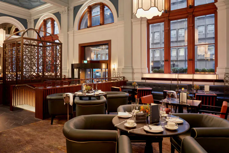 Elegant reimagined post office restaurant interior with arched windows, ornate screens, set tables, and pendant lights.