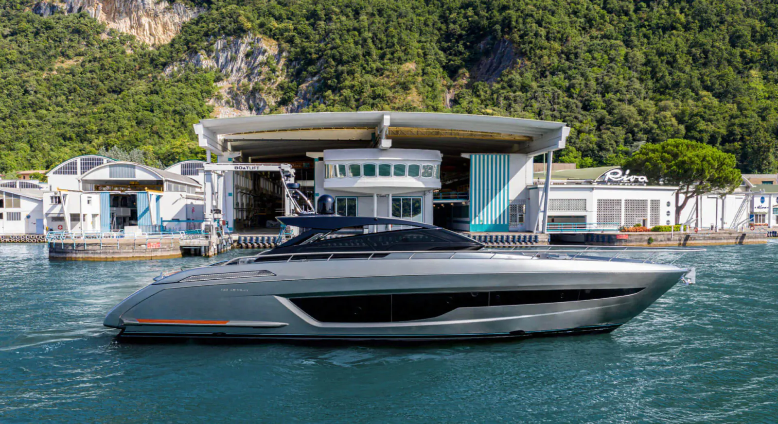 Sleek silver Riva 68’ Diable yacht docked at modern white boathouse by lush green cliffs and lake
