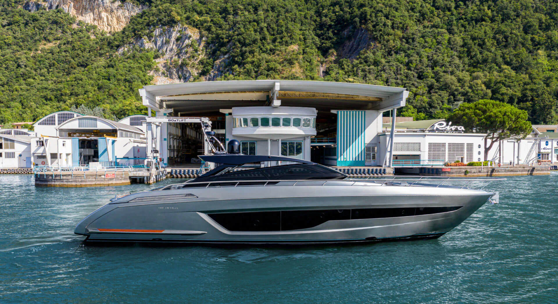 Sleek silver Riva 68’ Diable yacht docked at modern white boathouse by lush green cliffs and lake