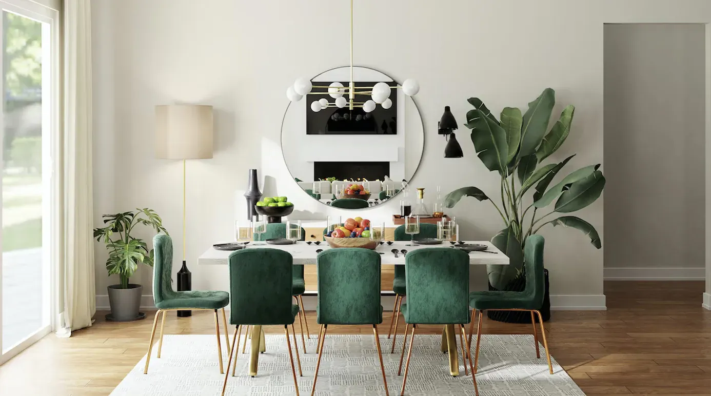 Modern dining room with green velvet chairs, round table set with fruits, large round mirror, plants, and chandelier.