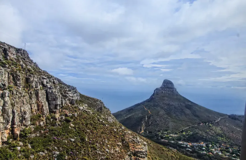 Table Mountain's prominent peak and rocky cliffs from cableway, with city below under partly cloudy skies