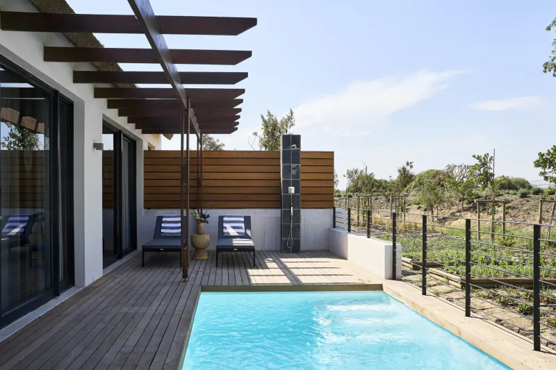 Modern white villa with wooden pergola, blue pool, loungers, and vineyard views at Stellenbosch estate