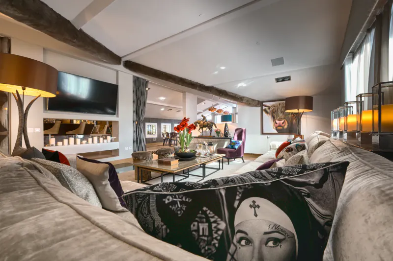 Luxurious mountainside chalet living room with modern sofa featuring Madonna print pillow, fireplace, red flowers, and large TV.