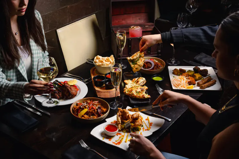 Three people sharing Indian dishes like naan, curries, and kebabs at Mint Leaf London restaurant table