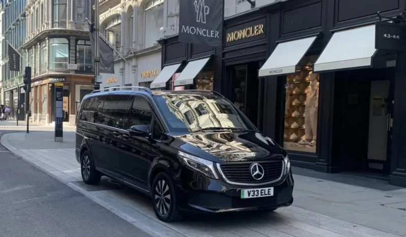 Black Mercedes-Benz V-Class limousine (YG23 EJE) parked outside Moncler luxury store on upscale city street.